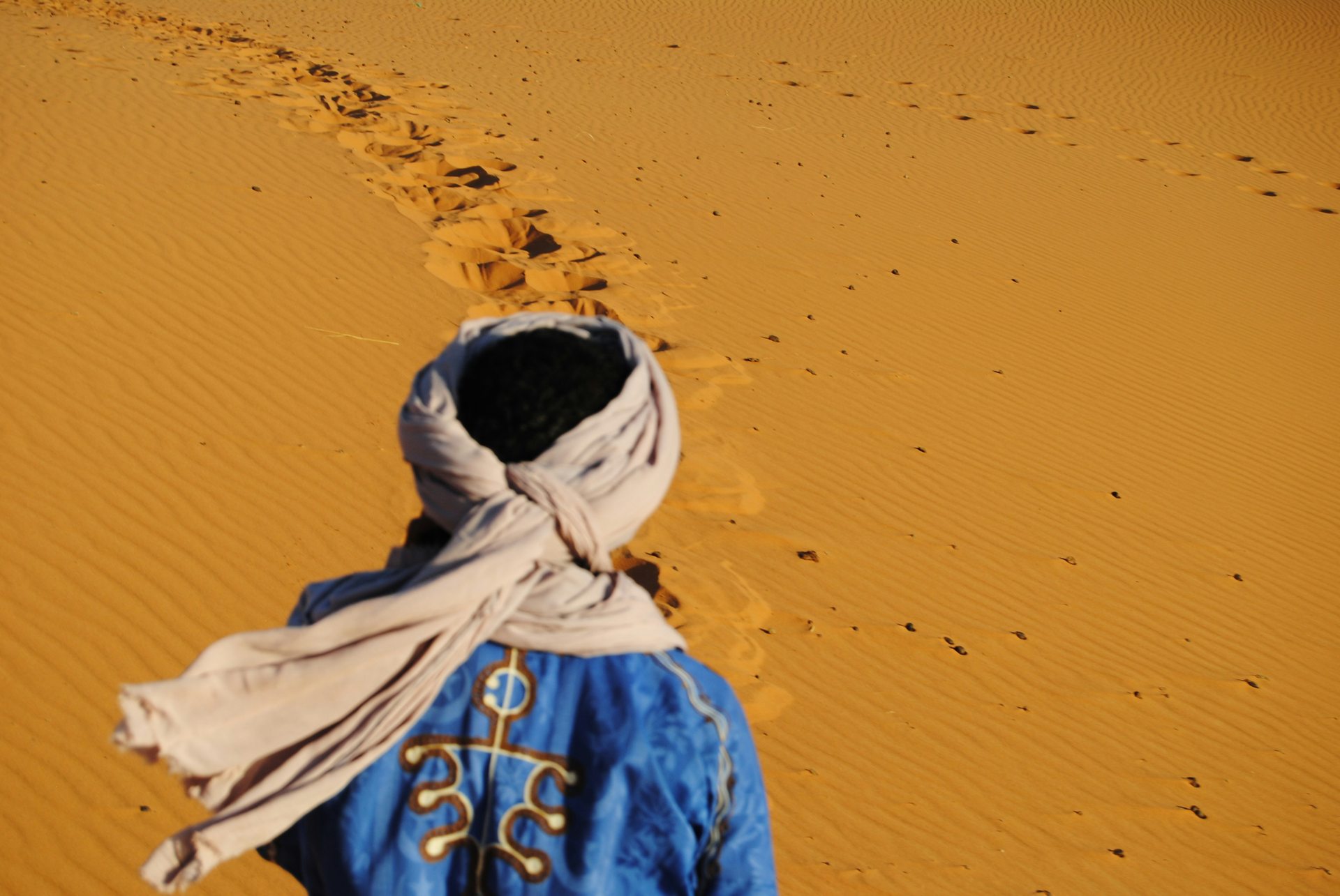A person wrapped against the sun walking through the Sahara desert