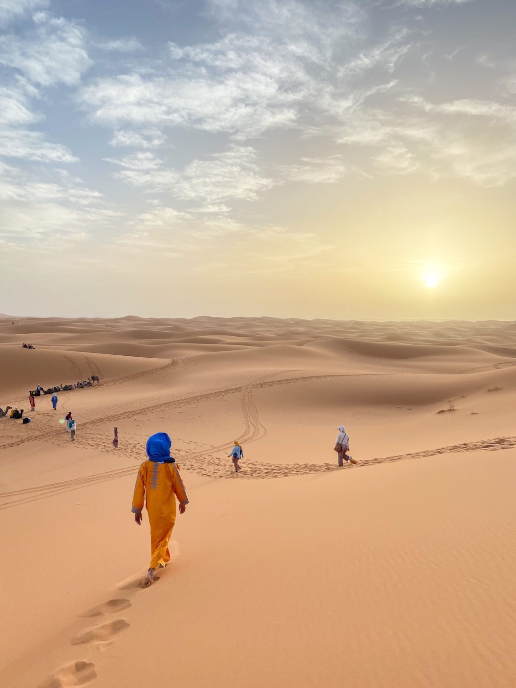 Travelers walking through the vast Merzouga dunes at sunset